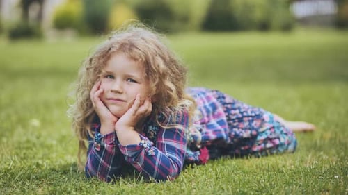 A Little Curlyhaired Girl Lies on the Grass in the Garden