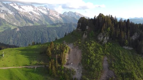 Drone Shot of Rugged Pine-Covered Mountain revealing a Snowy and Rocky Mountain Range in the Backgro