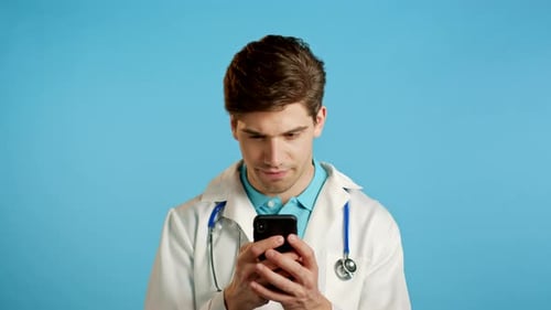 Apuesto médico con bata médica usando teléfono móvil, enviando mensajes de texto en Messenger y recibiendo SMS