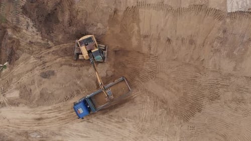 Aerial top view: yellow excavator pouring soil into tipper.
