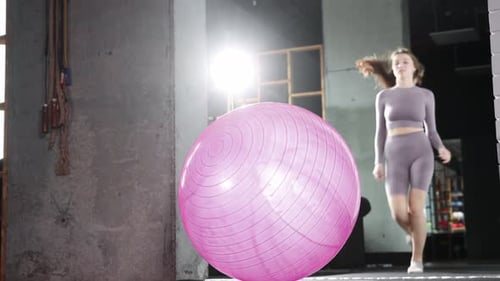 Young Woman Doing Pilates Running to the Fitness Ball and Sits Down on It