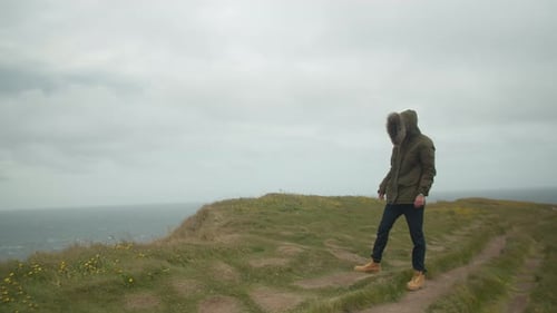 Caucasian Man Standing Near The Edge Of A Cliff In Iceland Coast During Windy Stormy Day