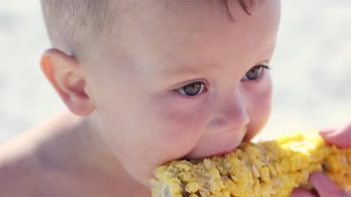 Happy Child Eating Corn on the Cob at Beach