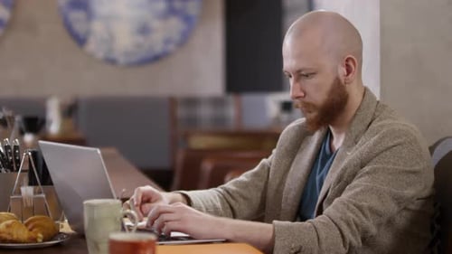 Geschäftsmann tippt beim Frühstück im Café auf Laptop