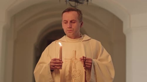 Priest with Burning Candle and Rosary Beads Walking along Church