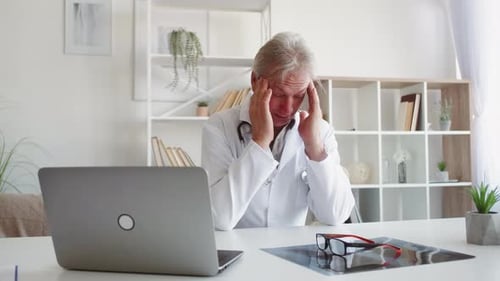 Stressed Doctor Massages Temples at His Desk