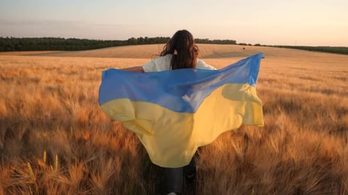 Woman Walks Through Wheat Field with Flag at Sunset