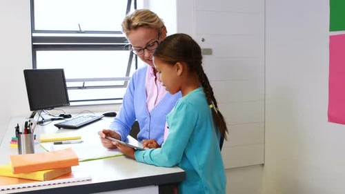 Teacher and schoolgirl using digital tablet in library