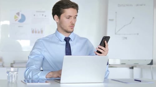 Young Adult Using Phone and Laptop in Office