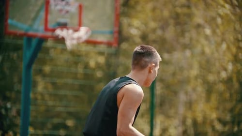A Man Standing on a Sports Ground and Holding a Basketball Ball - Throwing the Ball in the