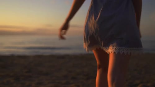 Schließen Rückseitenansicht einer jungen Frau, die am Strand auf See läuft und dabei ein blaues Sommerkleid trägt