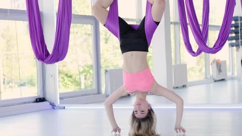 Woman doing aerial yoga suspended upside down indoors