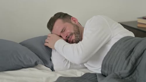 Hombre llorando mientras duerme en la cama