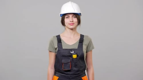 Portrait of Smart Young Woman Engineer or Builder in Helmet and Jumpsuit Smiling While Working on