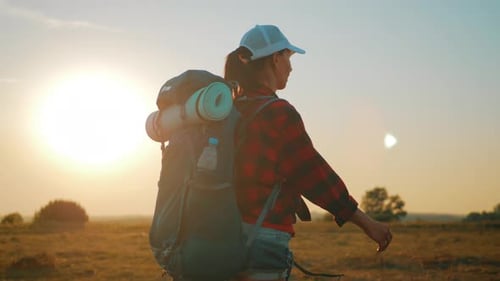 Female Hiker Walking in Grassy Field at Sunset