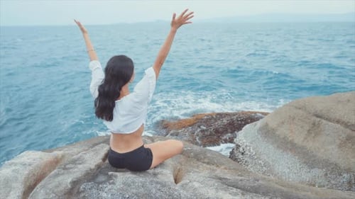 Woman Lifting Her Hands in the Air and Then Together While Meditating By the Ocean