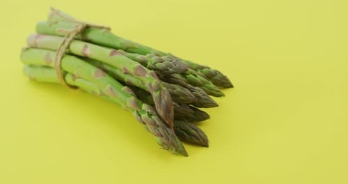 Video of close up of bundle of fresh asparagus over green background