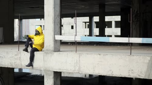 Mann mit Gasmaske und gelbem Schutzanzug sitzt am Rande des Abgrunds in einem unvollendeten verlassenen Gebäude