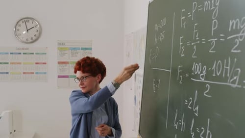 Teacher Writes Physics Equations on Chalkboard in Classroom