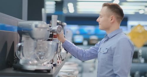 A Man Chooses a Blender in the Appliances Store Kitchen Appliances in His Hands and Considers the