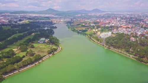 Flycam Moves Over Lake with Woods and City on Banks