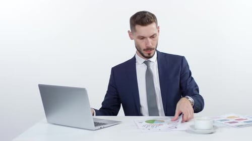 Businessman Looking Over Documents and Drinking Coffee