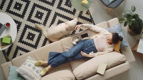 Woman Lying on Sofa and Petting Dog