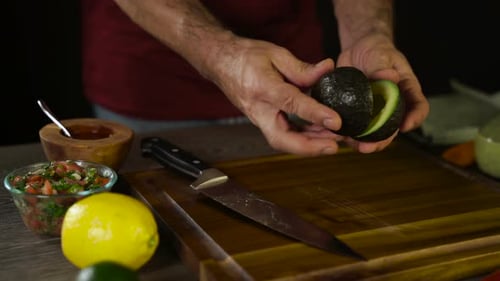 Man Cuts Avocado in Half on Wood Board