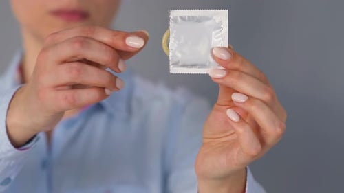 Woman Hands Holds and Unwraps Condom Close Up