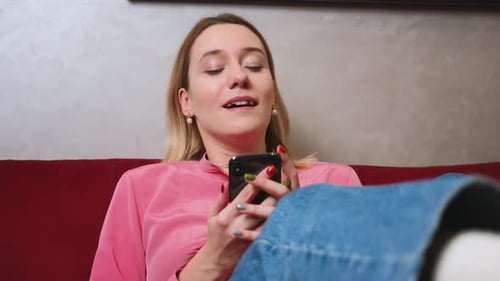 Stock Video Happy Young Woman Relaxing on Cozy Couch Using Smartphone