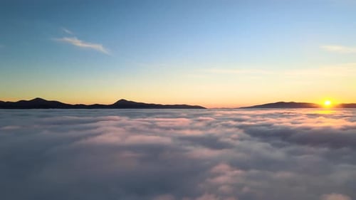 Aerial View of Vibrant Yellow Sunrise Over White Dense Clouds and Distant Mountains on Horizon