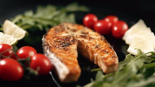 Ein gekochtes Lachssteak mit aromatischen Gewürzen und Gemüse auf einem schwarzen Servierteller