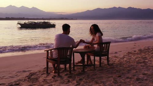 Beautiful young couple talking on quiet exotic beach at romantic moments of sunset reflecting on cal