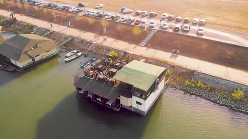Wooden house restaurant on the Danube river on an autumn sunny day. Aerial drone orbiting footage of