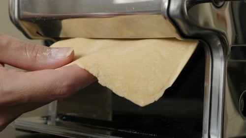 Pasta Dough Being Rolled Through Metal Machine