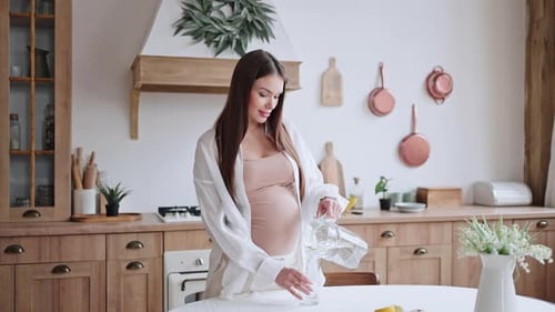 Pregnant Woman Pours and Drinks Water in Kitchen