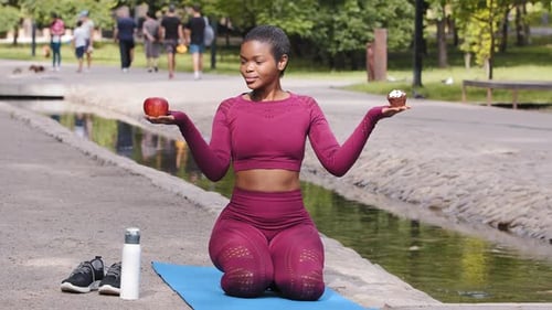 Atractiva instructora de fitness joven adulta sentada en una colchoneta de yoga en un parque de verano con capacidad para manzana