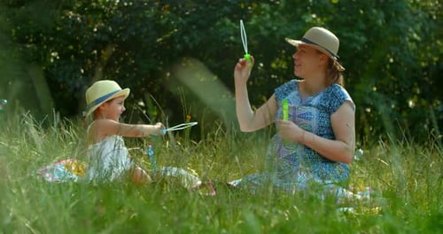 Mother and Daughter Blow Soap Bubbles in the Park