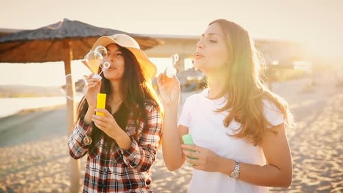 Women Blowing Bubbles on Beach at Sunset