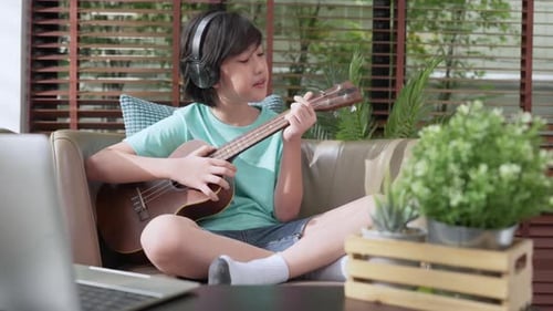Boy Plays Ukulele on Couch at Home