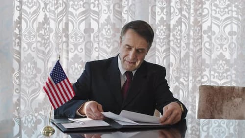 Man in Suit Reviews Documents at Table