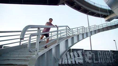 ein Freerunner springt von einer hohen Leiter auf Kies vor dem Hintergrund von Graffiti unter einer Brücke