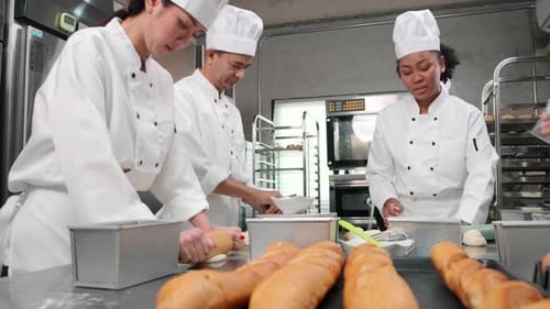 Chefs team in uniforms prepare to bake bread and pastry in stainless kitchen.