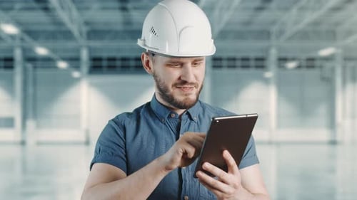 A Man Construction Worker with Helmet is Smiling and Using Tablet at Building Site