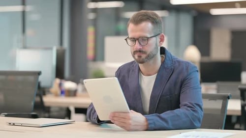 Middle Aged Businessman Browsing Internet on Tablet While Sitting in Office
