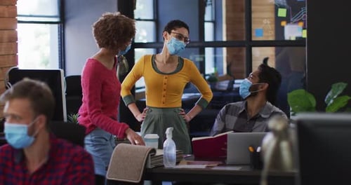 Diverse colleagues wearing face masks discussing together at modern office