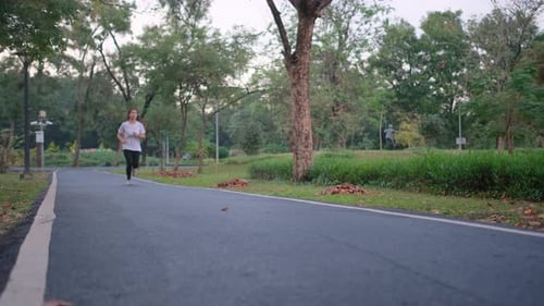 Front view of Asian sport woman is jogging on road in green park with evening light