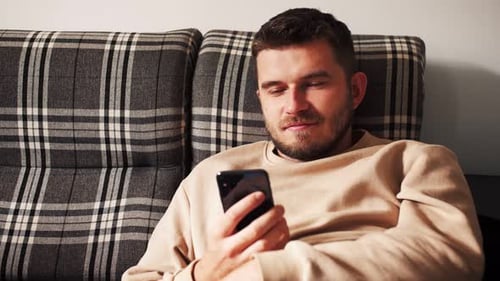 Man Using Smartphone Smiling on Plaid Couch