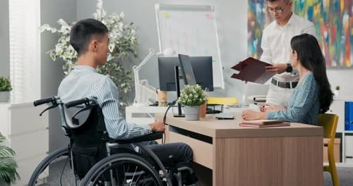 A Man Sits in a Wheelchair at a Desk in an Office Across From Him a Beautiful Woman in a Dress They