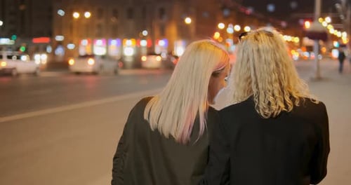 Blonde Friends Walk Along Street and Laugh Against Lights